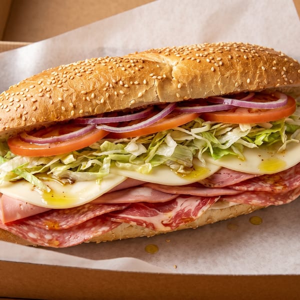 A large deli sub sandwich with various meats, cheese, lettuce, tomatoes, and onions in a box.